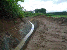 山と地面の境目の明渠に掘られた排水路の整備工事の現場の写真