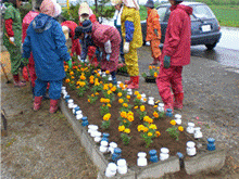 レインコートを着た人たちが花壇に花を植えている写真