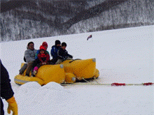 雪が積もった緩やかな傾斜で黄色のボートに乗って楽しんでいる人達の写真