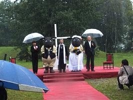 雨の降る中檀上に立つさほっち（羊田黒助くん）とメイちゃん（羊野メイさん）と神父さんたちの写真