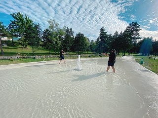 2名の方が地面から噴き出している水の周りで遊んでいる様子の写真
