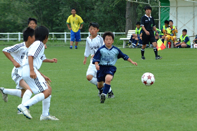 チームのユニフォームを着た子供たちがサッカーボールを追い掛けている少年サッカー大会の様子の写真