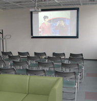 前方のスクリーンに映像が映し出されており、椅子が並べられた展示室（AV装置等）を写した写真