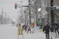 雪が積もっている道路の歩道で投雪作業している人たちの写真