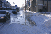 雪が溶けて水が溢れる道路を走る車の写真