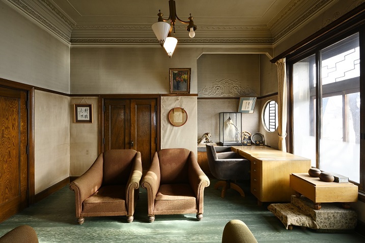 窓に面して机と椅子、その横に囲碁の碁盤が置かれ、部屋の中央には一人掛け用のソファが2脚置かれている写真