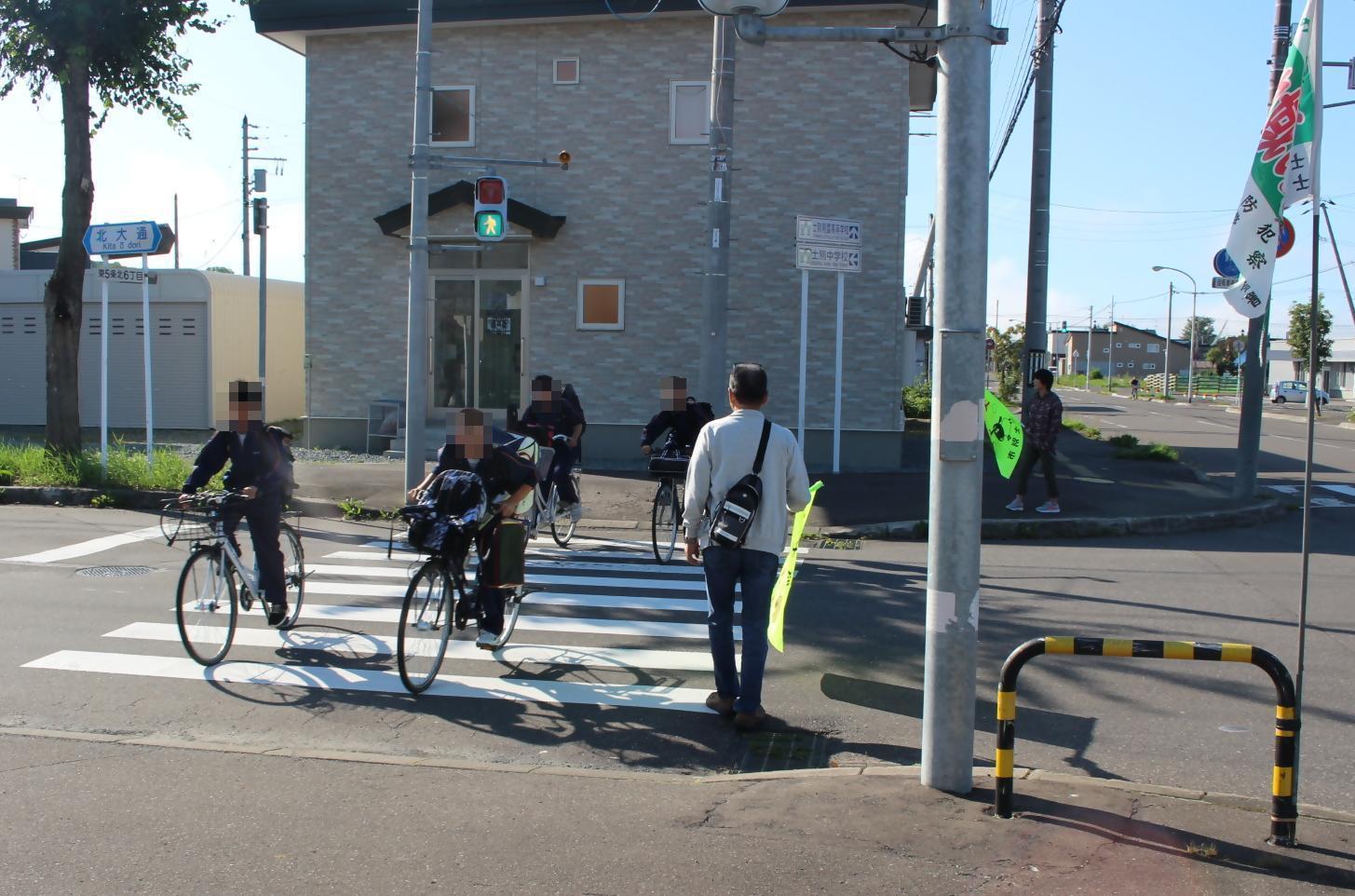 北地区の交通安全見守り活動として自転車に乗る生徒を見守る地域住民
