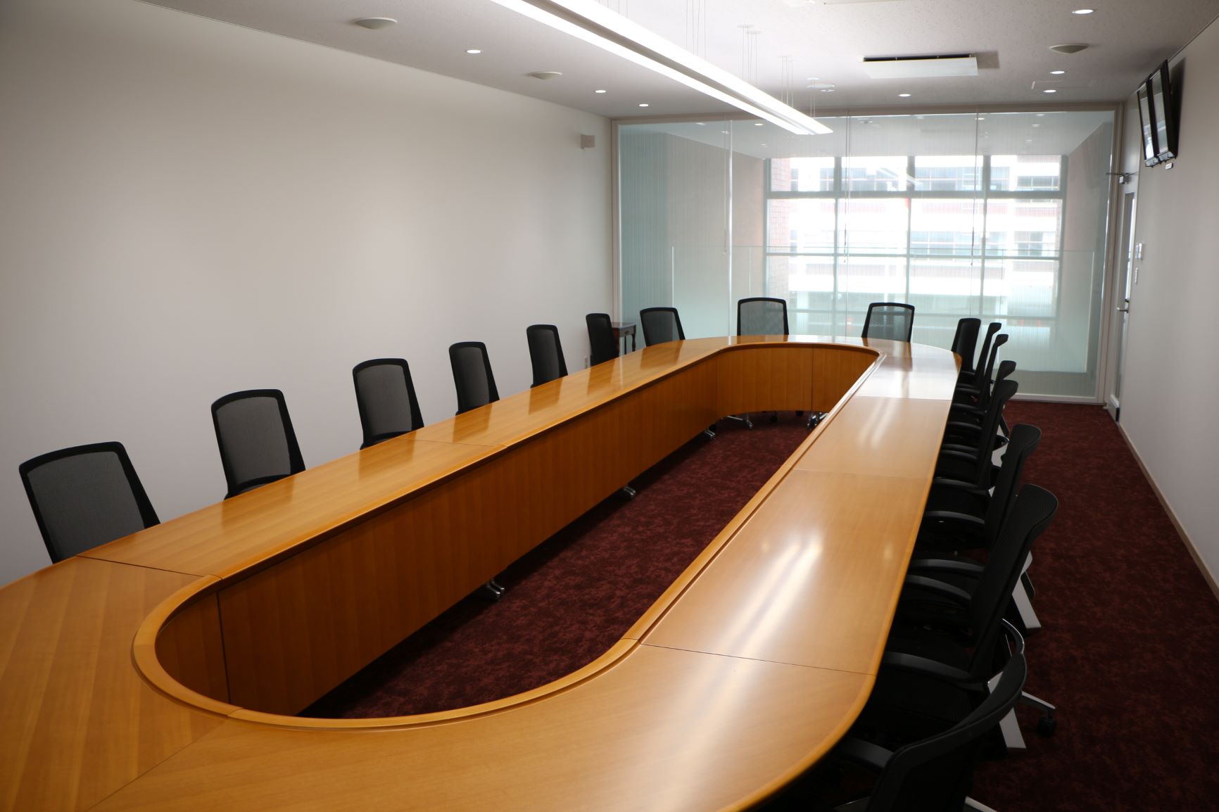奥にすりガラス状の壁、手前に縦に長いO字型の木製のテーブルに黒色の椅子が設置されている庁議・来賓室の写真