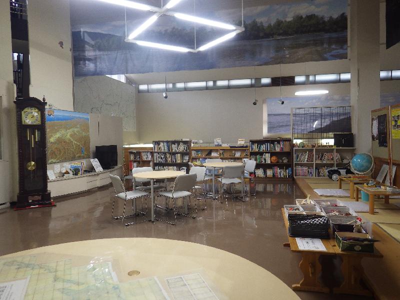手前に地図が貼られた大きな円卓、右側に畳コーナー、奥に図書資料コーナーが見えるエントランスホールの写真