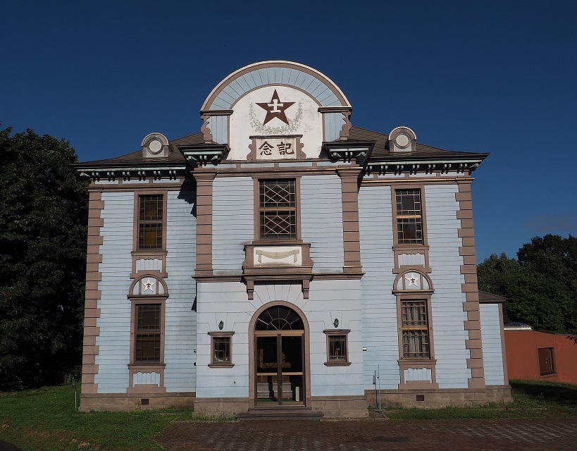 水色を基調とした2階建ての建物の上の部分のに星型に「士」と書かれたエンブレムがのっている公会堂展示館の外観写真