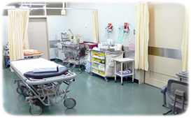 中央にストレッチャーが置かれており、壁際に治療用の道具が並べられている救急外来診療室の写真