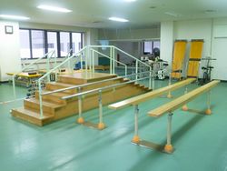手すりのついた短い階段や、スロープなどが置かれている機能回復訓練室の写真