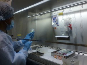クリーンウエアを着た男性が、アンプルの薬液をルアーロックシリンジで吸引している無菌製剤混合業務の写真