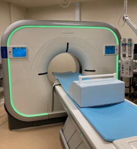 中央に大きな輪があき周囲が緑色に光っている架台に患者が横たわる寝台が設置されたCT検査室内の写真