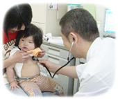 お母さんが抱いて座っている子どもの胸の音を聴診器で聞く医師の写真