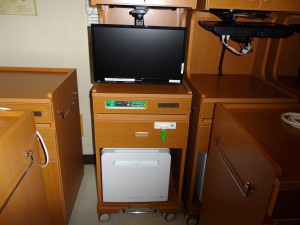 木製の茶色い床頭台の上に液晶テレビ・床頭台の下部に設置された白い冷蔵庫の写真