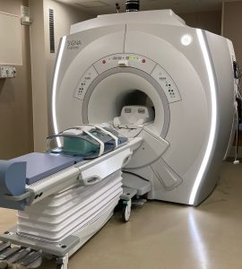 中央に大きな輪があいている架台に患者が横たわる寝台が設置されたMRI検査室内の写真
