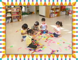 5人の子ども達が近くに集まり、色とりどりの紙のようなもので遊んでいる様子の写真