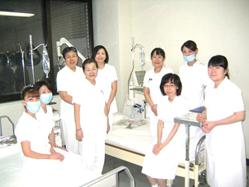 2台のベットと透析の機械のある部屋に集まっている9名の看護師のスタッフの皆さんの集合写真