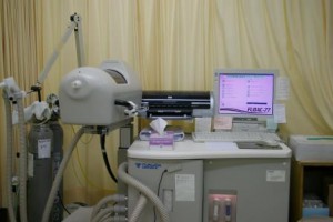 台の上にパソコンとプリンターが置かれ、左側にホースに繋がった機械と2本の細いガスボンベが設置されている肺機能検査の機器の写真