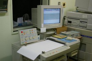 パソコンのディスプレイに波形が表示され、下に設置された機械から用紙が出力されている脳波検査の機器の写真