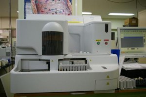 右側にパソコンのディスプレイが設置され、左側に緑色と赤色のボタンがついている横幅約2メートルくらいの血液凝固線溶検査の機器の写真