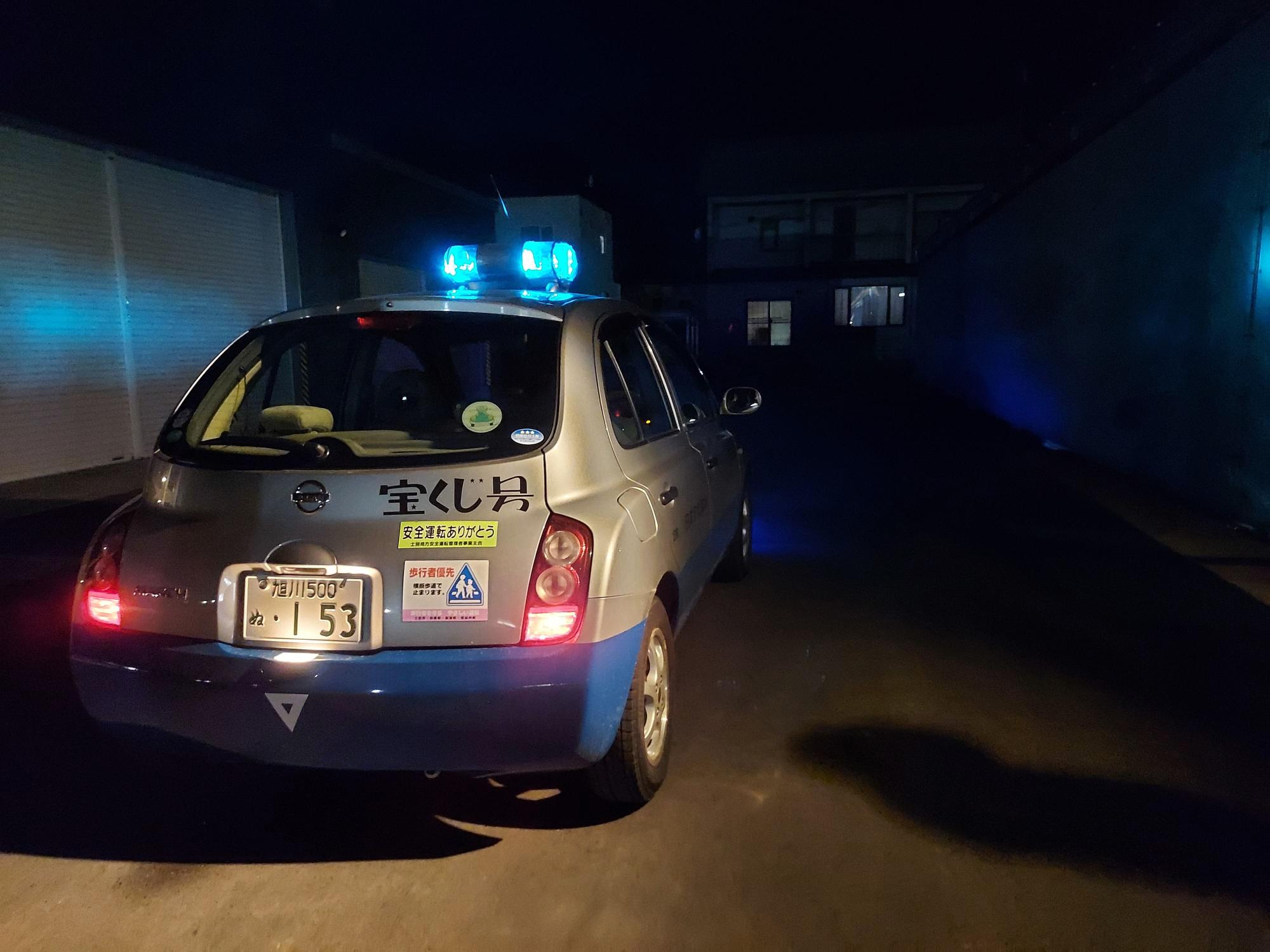 車のルーフ部分につけられた青色のパトランプを回し夜道を走行している青色防犯パトロール車の写真