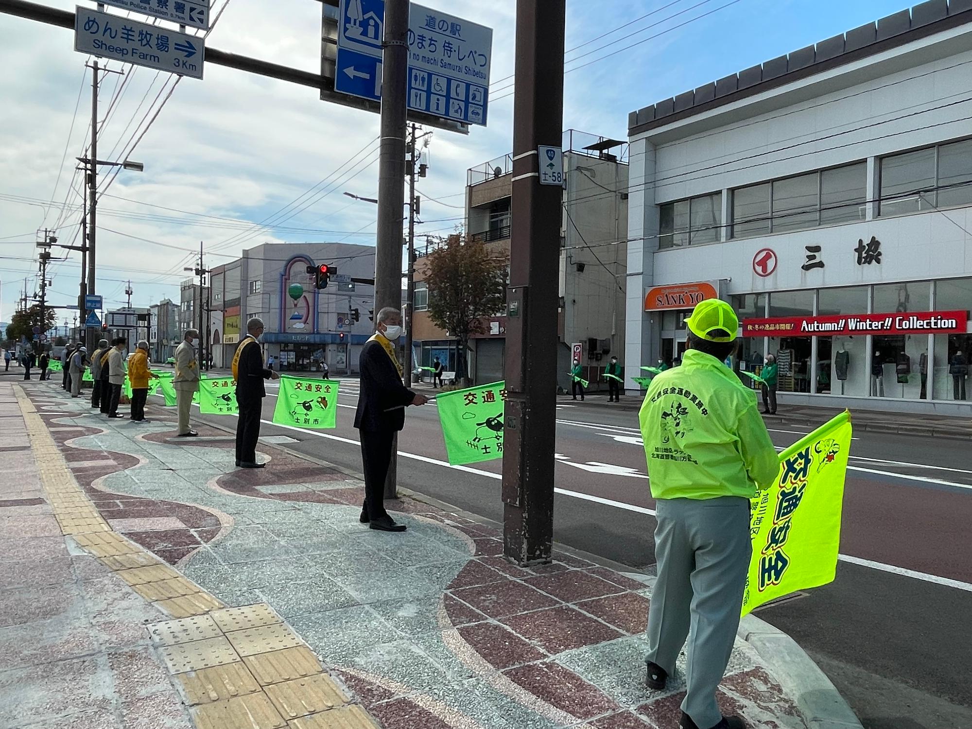 交通安全の旗を掲げ通過する車両にスピードダウンを呼び掛けている写真