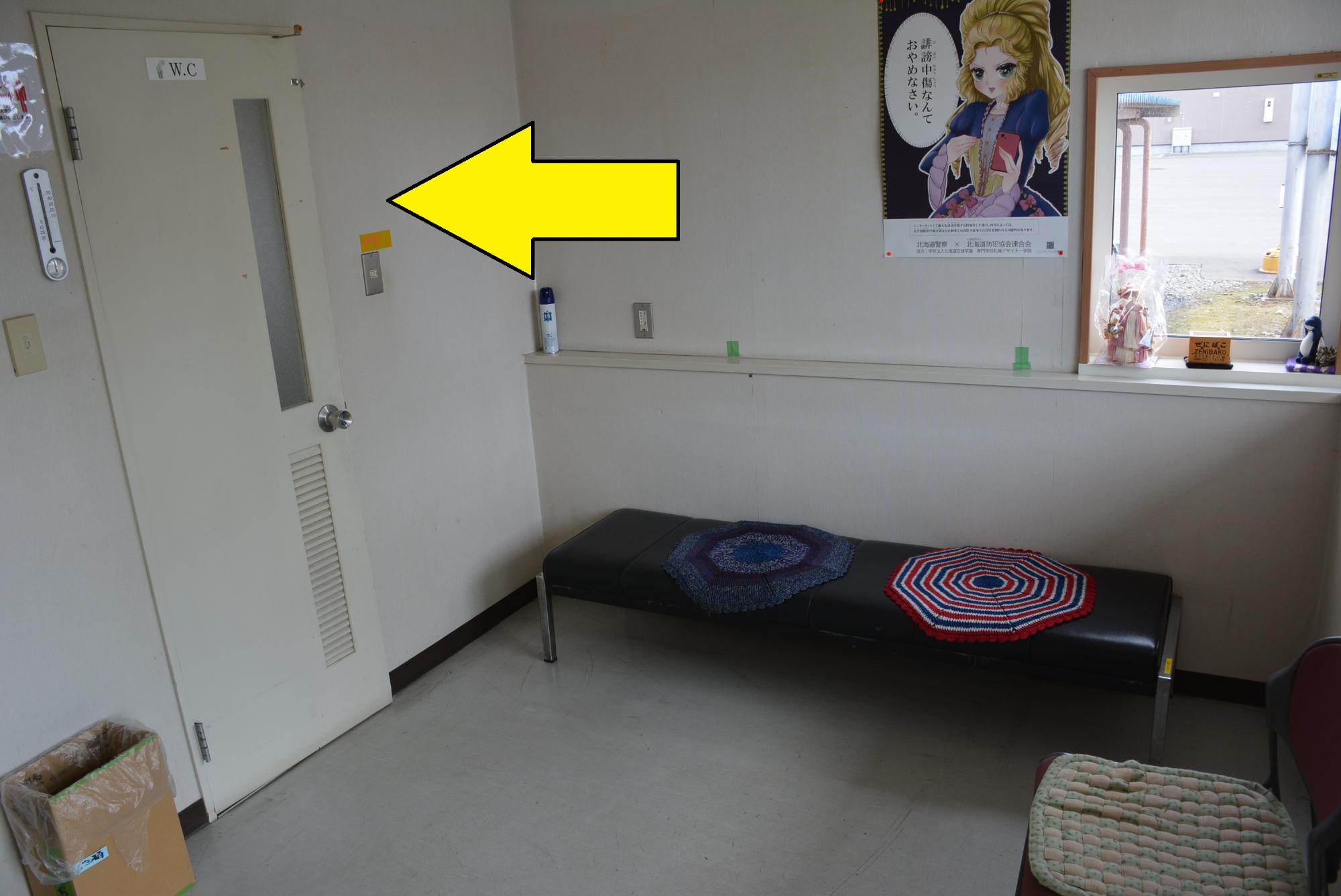 壁にポスターが掲示され、黒い長椅子があり、トイレの場所を矢印で示した写真