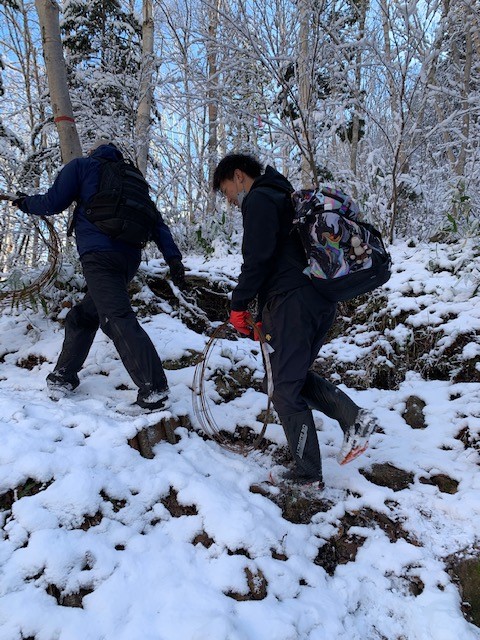 雪の降り積もった山中を登っている紙谷隊員と職員の方の写真
